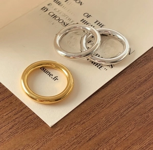 Three minimalist S925 sterling silver bands in gold and silver finishes on a desk
