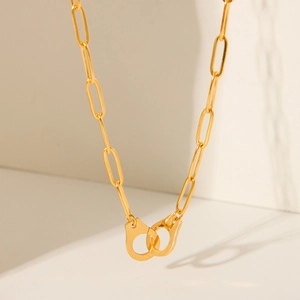Golden paperclip chain necklace with interlocking handcuffs pendant on white background