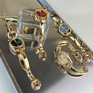 Luxury gold chain jewelry watches with colorful dials displayed on reflective surface