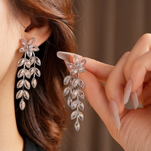 Close-up of silver tassel earrings with crystal leaf motifs and flower studs on model