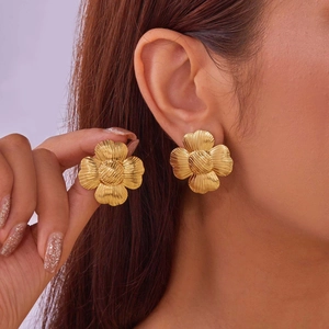 Detail of large gold ginkgo leaf stud earring showing brushed metal texture and 3D floral petals