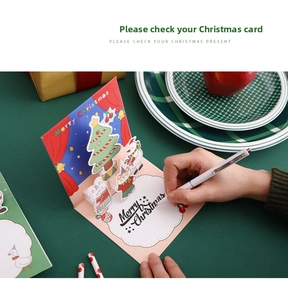 Close-up of handwriting on a 3D pop-up Christmas card with festive tree and snowman scenes