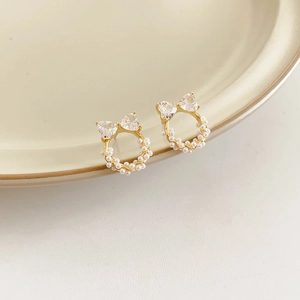 Détail de boucles d'oreilles nœud en perle, métal doré et zircons sur plat céramique