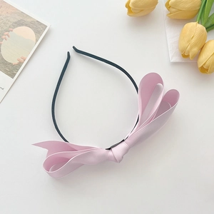 Detail showing the pink satin bow texture and black thin headband on white background