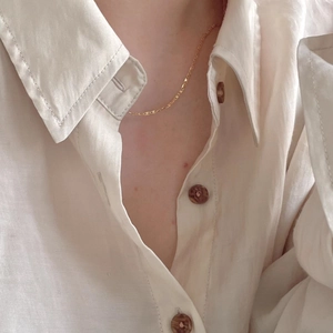 Close-up of minimalist gold 925 sterling silver chain necklace on white linen fabric