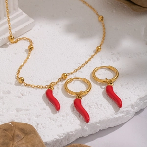 Close-up of gold 18K plated necklace and red chili earrings on white stone display
