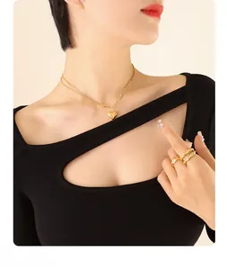 Close-up of double-layer gold heart necklace and stacked rings on a black outfit
