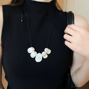 Detail of irregular white resin pendants on black leather cord necklace worn on model