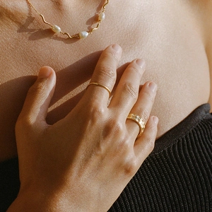 Close-up of a gold necklace with white pearl and layered gold rings on a model