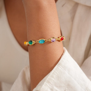 Close-up of a gold link bracelet featuring colorful oval resin stones on a model wrist