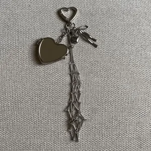 Detail of silver heart charm with metallic bow and long tassel on grey fabric