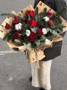 Close-up of Christmas bouquet with red roses and pine needles in kraft paper wrap