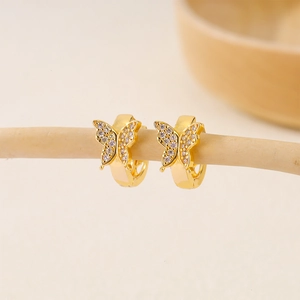 Macro view of gold butterfly hoop earrings with white zircon accents on a branch