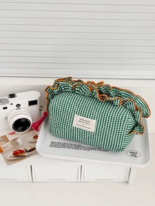 Detailed view of green checkered quilted makeup bag with orange ruffles and pink tassel