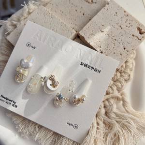 5D embossed press-on nails with cream white base, pearls, and metallic bow accents