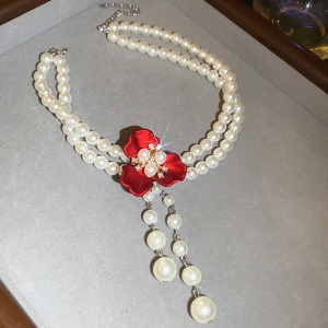 Detail view of double-layer pearl necklace featuring a red flower pendant and pearl tassels
