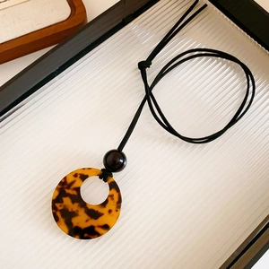Detail of an irregular leopard print resin pendant on a minimalist black cord necklace