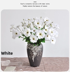 Close-up of white silk ranunculus flowers in a black marbled ceramic vase on striped cloth