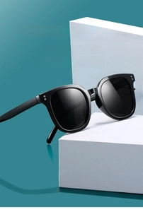 Detail of square black sunglasses with silver rivet accents on a white display block