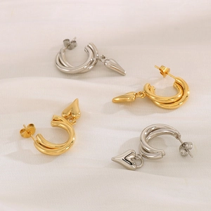 Macro detail of gold and silver double-hoop C-shaped earrings with heart pendants