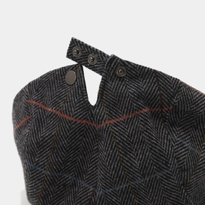 Detail of herringbone tweed flat cap featuring adjustable metal buckle and silver snaps