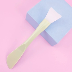 Detailed view of dual-ended silicone face mask brush with scraper on a blue stand