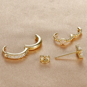Macro detail of gold-plated clover earrings and zircon hoops on champagne silk fabric