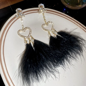 Detail of elegant gold earrings featuring a crystal heart and black feather tassels