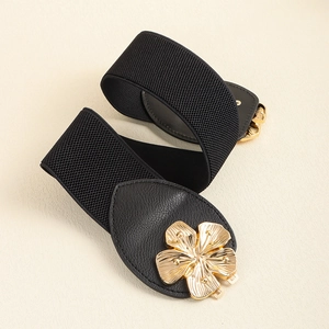 Detail of black elastic belt with golden peach blossom metal buckle on beige background