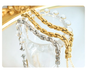 Macro shot of minimalist gold and silver curb chains hanging on a glass rim