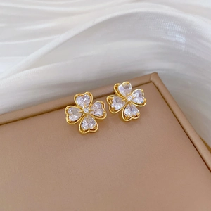 Close-up of gold clover stud earrings with four heart-shaped white zircons on silk