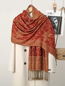 Detail of red paisley scarf with golden tassels and logo label on a white coat