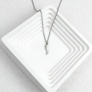 Polished silver stainless steel chili pendant necklace on a white minimalist display