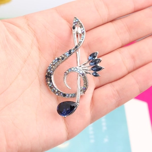 Detailed close-up of a silver music note brooch with blue crystals and sparkling rhinestones