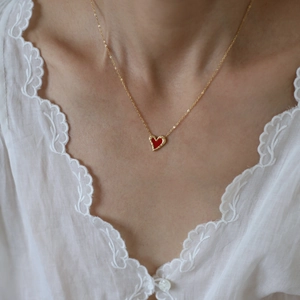 Close-up of heart necklace with gold chain and red pendant on model neck