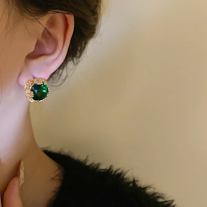 Dettaglio dell'orecchino con zircone verde smeraldo e placcatura dorata su una modella