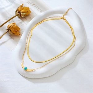 Detail of layered gold necklace with snake chain and turquoise wing pendant on white tray