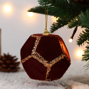 Red flocked Christmas ball with gold geometric glitter lines on a festive pine branch