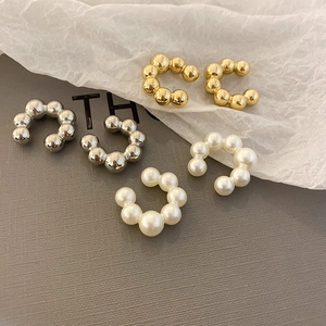 Dettaglio di ear cuff a forma di C in metallo dorato, argento e perle su sfondo grigio