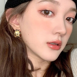 Minimalist wide golden C-shaped hoop earrings with polished mirror finish on female model