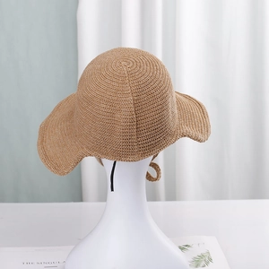 Detail of light brown straw sun hat featuring a wide wavy brim and black chin strap