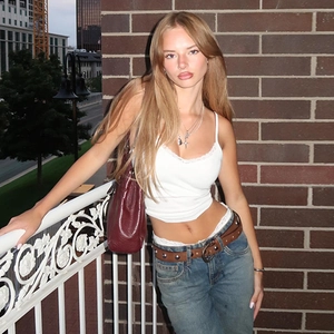 Close-up of white camisole with lace trim paired with blue jeans and red handbag