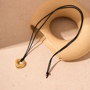 Detail of a minimalist gold hollow heart pendant on a black cord over a stone texture