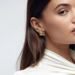 Detailed view of geometric square gold earrings with quilted texture on female model