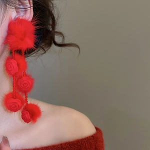 Detail view of red faux fur pompom earrings with elegant rose flower accents on a model