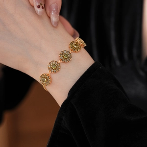 Macro shot of gold floral bracelet with green zircon petals on wrist over black fabric