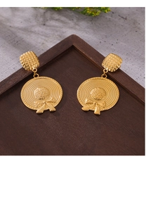 Macro detail of gold-plated straw hat earrings with bow accent on a wooden tray