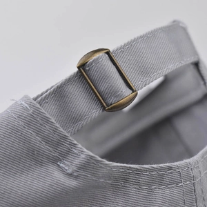 Detailed close-up of the vintage bronze metal buckle on a gray washed cotton baseball cap