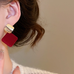 Gros plan d'un modèle portant des boucles d'oreilles carrées en velours bordeaux et or