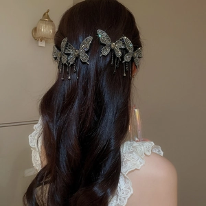Detail showing a rhinestone butterfly hair clip with tassel chains worn on an elegant updo